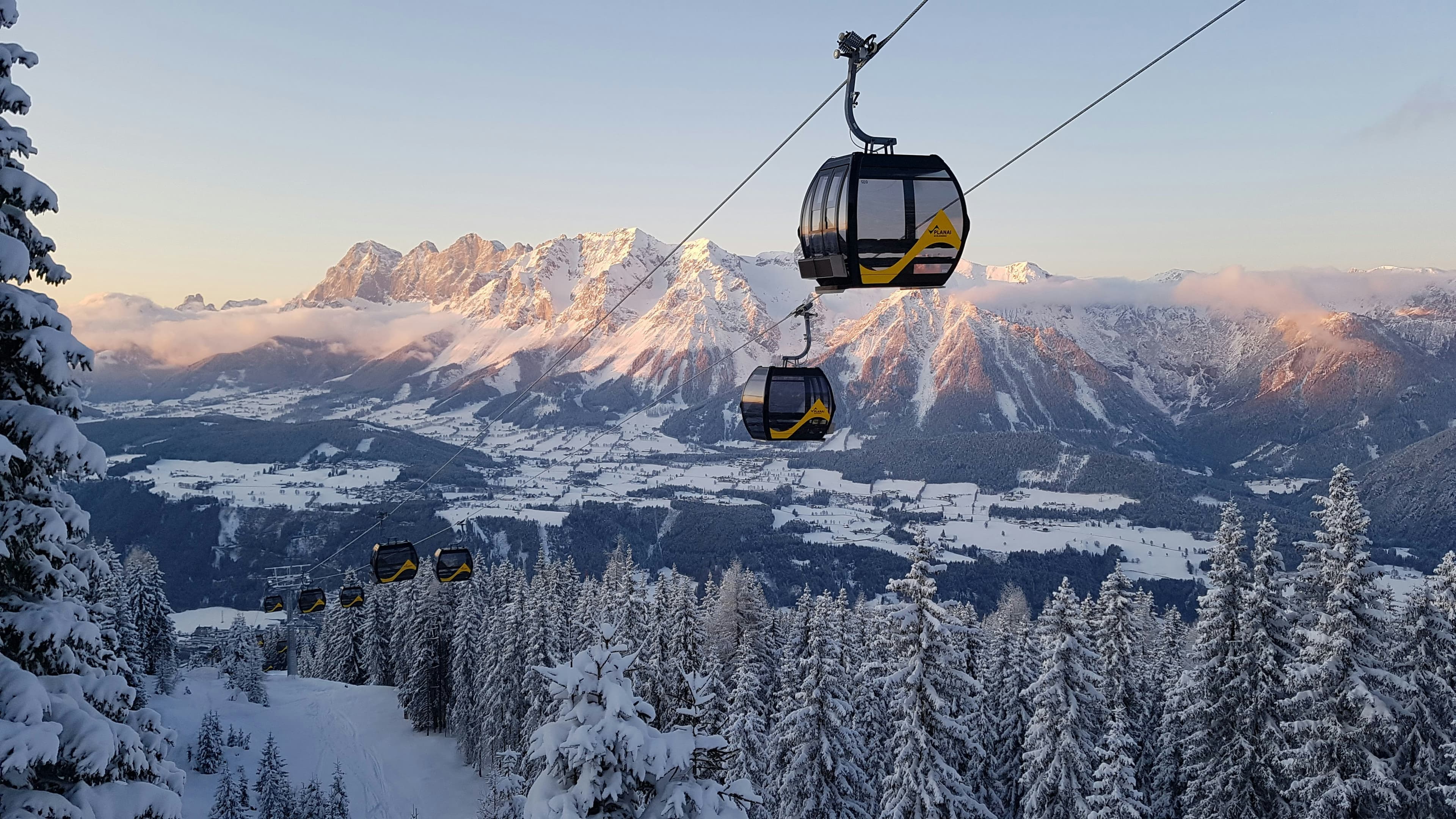 Gondel zweeft boven besneeuwde bossen met de Dachstein op de achtergrond
