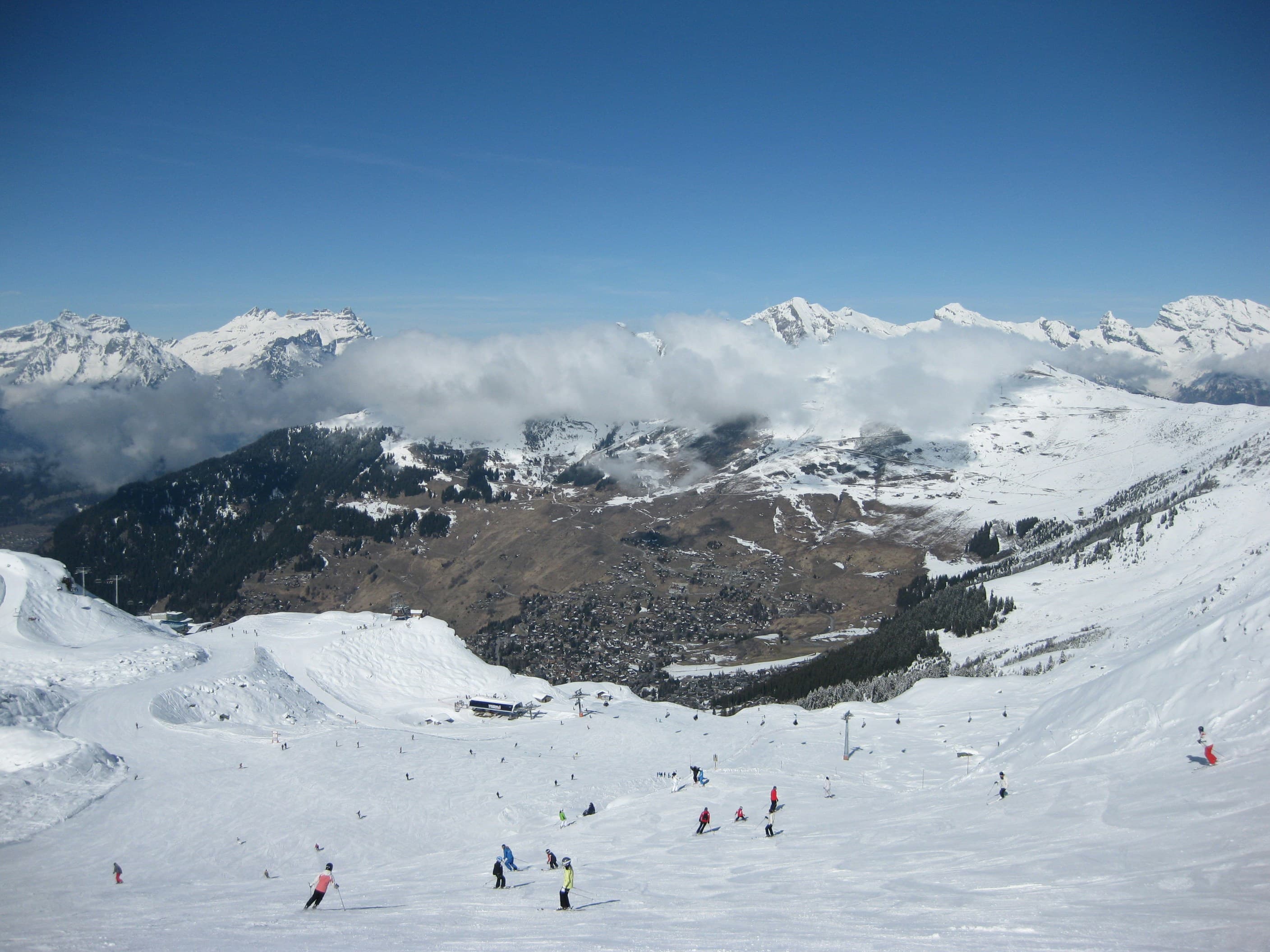 Skiërs op zonnige pistes boven het dal van Verbier