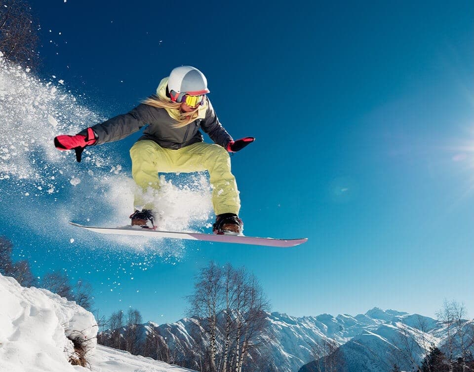 Snowboardster maakt een sprong onder een strakblauwe lucht in de Alpen